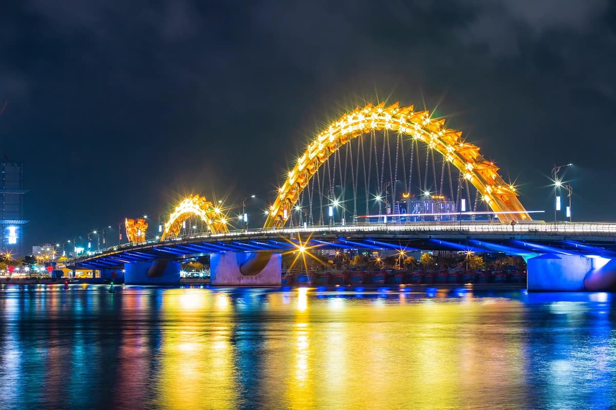 The Dragon Bridge in Da Nang glows orange and yellow at night with its giant dragon-shaped span illuminated above the Han River