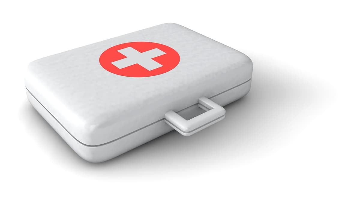 A travel first-aid kit laid out on a hotel desk with kid-strength Tylenol, Pedialyte packets, sunscreen, Picaridin spray, and a small thermometer