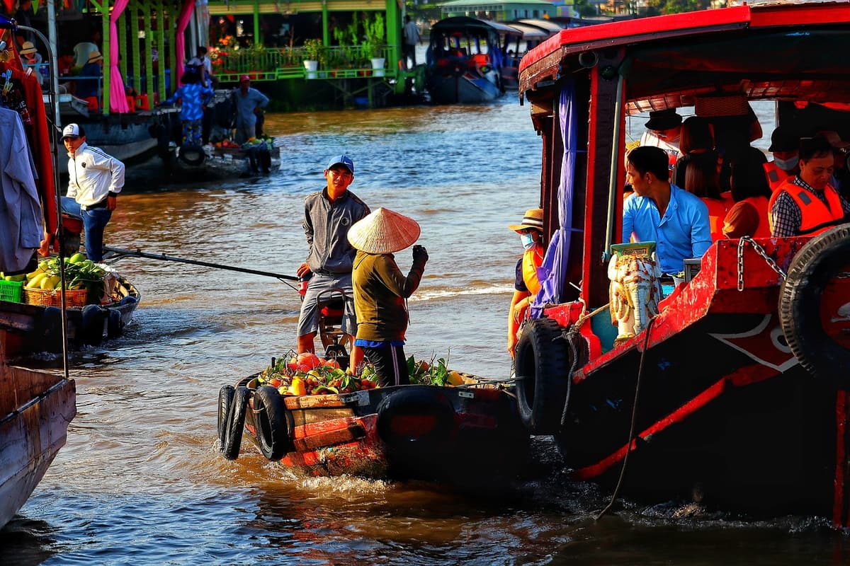 Vendors in conical hats arrange produce on small wooden boats at Cai Rang floating market under a pink sunrise sky