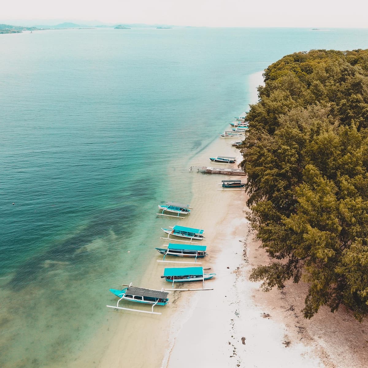 A small wooden tour boat anchors off a tiny green palm-covered islet in the An Thoi Archipelago with snorkelers floating in the clear blue water