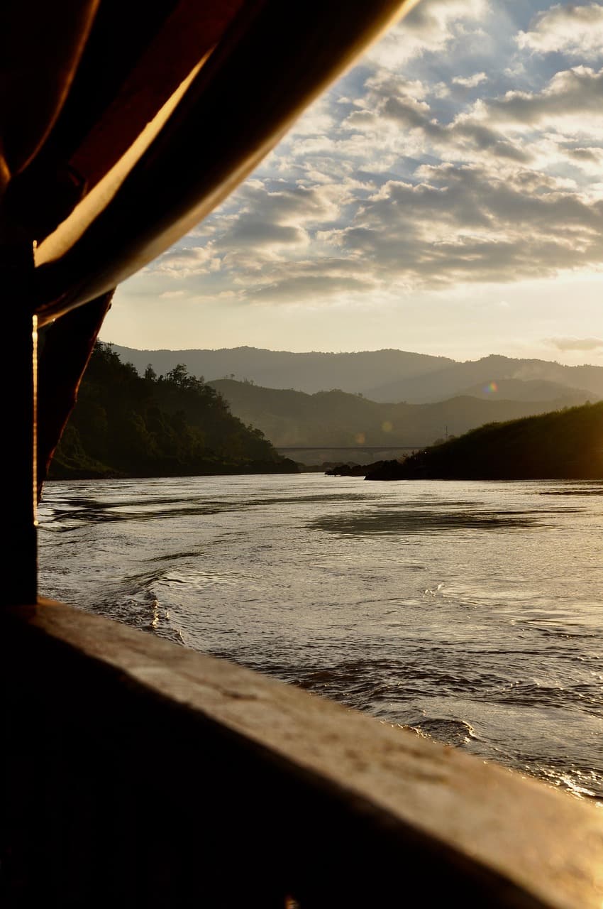 A wide curve of the Hau River in Can Tho reflects palm trees and a small wooden cargo boat under a soft morning sky