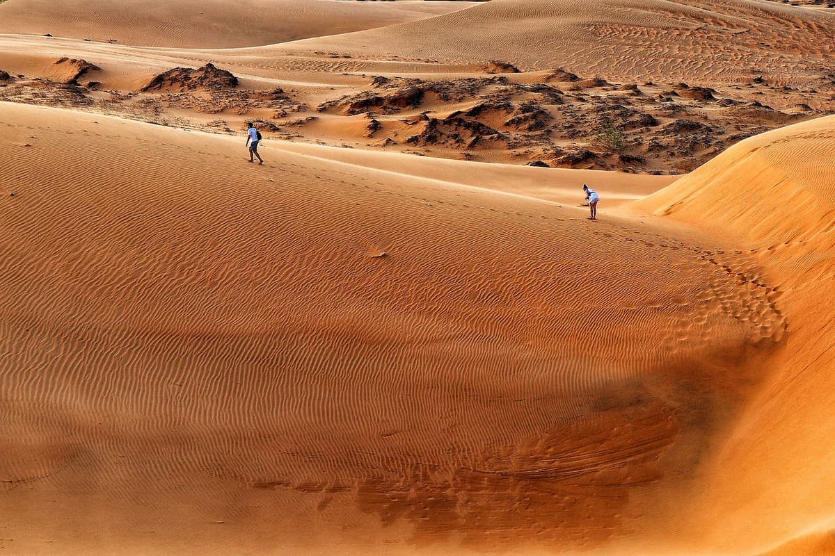Smooth ridges of red sand at Mui Ne's red dunes catch low golden light with a single figure walking along the crest